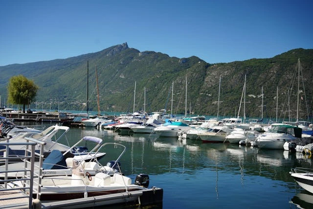 Marina pittoresca sul Lago di Bourget con barche a vela e yacht ormeggiati, circondata dalle maestose montagne delle Alpi francesi sotto un cielo azzurro perfetto nella regione Alpi Marittime"