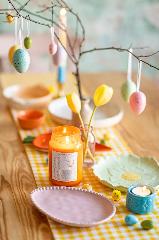 Tradizioni Pasqua: albero decorativo con uova colorate appese, centrotavola festivo con candele, tulipani gialli e piattini pasquali