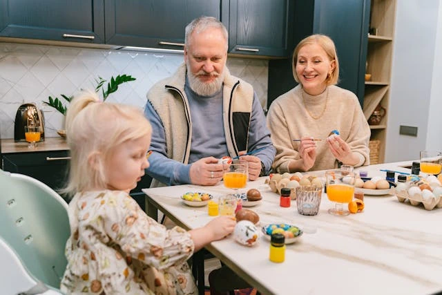 Tradizioni Pasqua in famiglia: nonni e nipotina decorano insieme uova pasquali colorate al tavolo della cucina durante i preparativi festivi