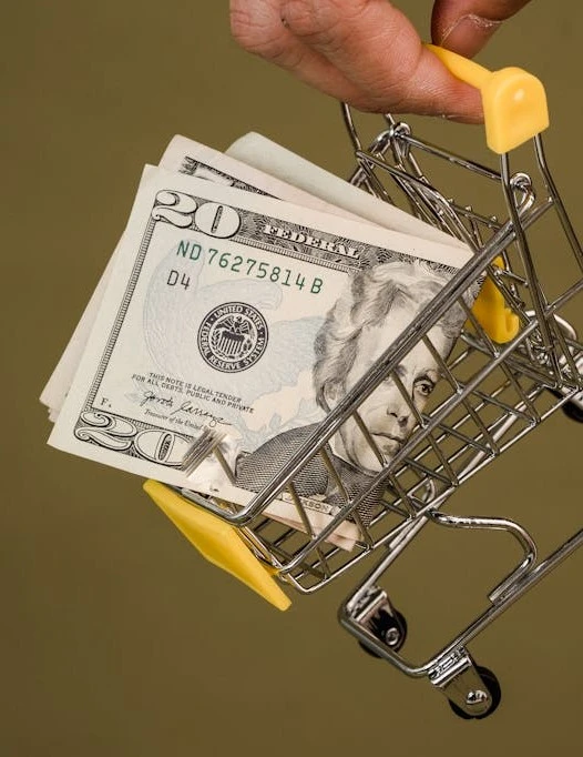 Spesa consapevole: mini carrello con denaro simboleggia il risparmio economico nella pianificazione degli acquisti alimentari