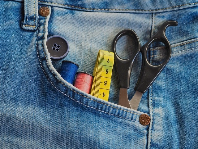 Tasca posteriore di jeans con ago, filo e strumenti da cucito: simbolo di riparazione, creatività e moda circolare.